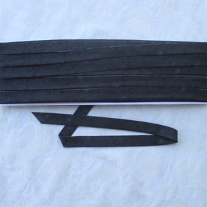May include: Black fabric ribbon with a subtle textured pattern. The ribbon is folded and stacked on a white surface.