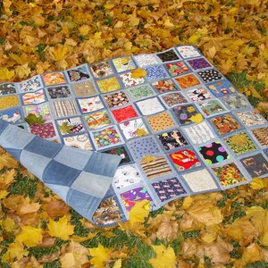 May include: A patchwork quilt made from denim squares with different fabric patterns and colors. The quilt is lying on a bed of fallen autumn leaves.