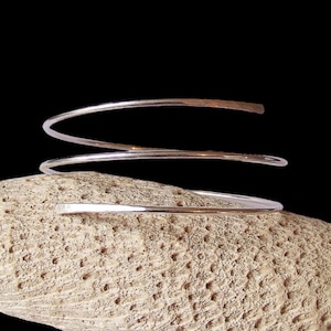 May include: A silver bangle bracelet made of three thin, twisted wires. The bracelet is open and has a simple, minimalist design.