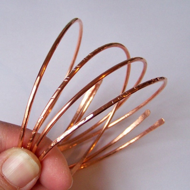May include: Five copper wire bracelets stacked on top of each other. The bracelets are all the same size and have a hammered texture.