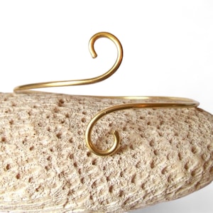 Peut inclure: Un bracelet en métal doré au design simple et élégant. Le bracelet a une forme incurvée et présente deux petites extrémités recourbées.
