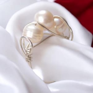 May include: A silver wire bracelet with three white pearls. The bracelet is on a white fabric background.