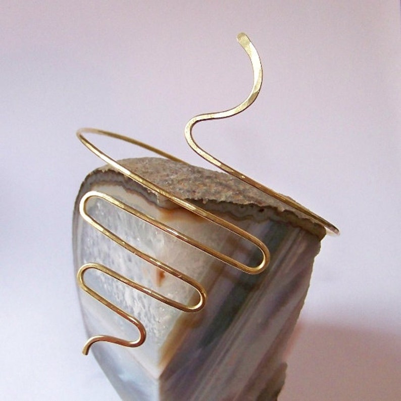 Pu&ograve; includere: Un cerchietto in metallo dorato con un design astratto unico. Il cerchietto &egrave; realizzato con un unico filo di metallo piegato in una serie di curve e anelli.
