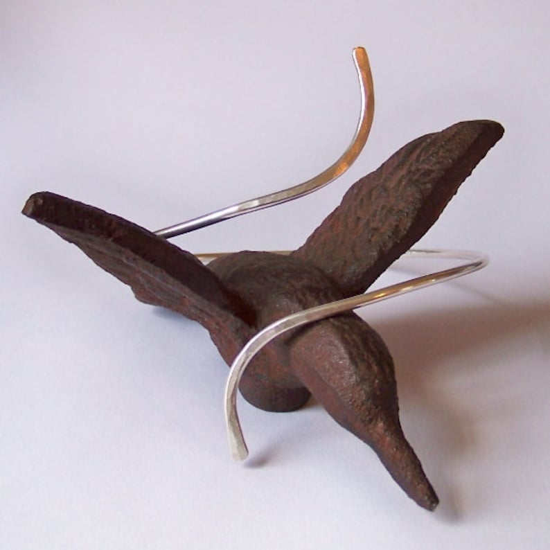 May include: A silver metal bracelet with a unique design. The bracelet is made of two pieces of silver wire that are twisted together. The bracelet is displayed on a brown, bird-shaped object.