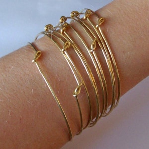 May include: A set of gold-toned bangle bracelets with a knotted design. The bracelets are stacked on a person's wrist.
