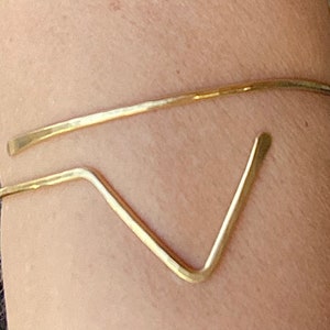 Puede incluir: Un brazalete de metal dorado con un diseño en forma de V.