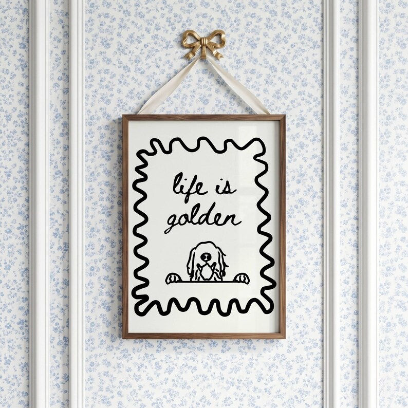 May include: A rectangular wall art print in a brown wooden frame, featuring a black wavy border on a white background. The text reads "life is golden" above a line drawing of a dog peeking over a ledge. A cream ribbon and gold bow hang it.