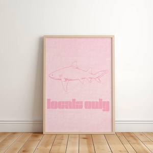 Op de afbeelding: Roze en witte poster met een roze omtrek van een haai en de tekst "locals only" in roze letters.