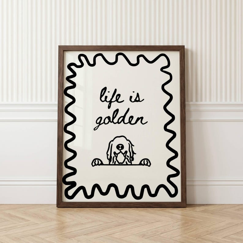 May include: A framed wall art print featuring a cream-colored background with a thick black wavy border. The text "life is golden" is written in black cursive script above a simple black line drawing of a dog peeking over a horizontal line.