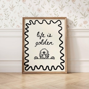 May include: A framed wall art print featuring a cream-colored background with a black wavy border. The text "life is golden" is written in black cursive script above a black line drawing of a dog peeking over a horizontal line.