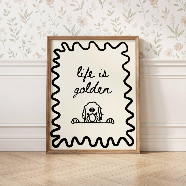 May include: A framed wall art print featuring a cream-colored background with a black wavy border. The text "life is golden" is written in black cursive script above a black line drawing of a dog peeking over a horizontal line.