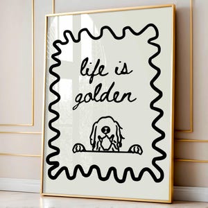 May include: A framed wall art print featuring a cream-colored background with a black wavy border. The text "life is golden" is written in a black cursive script above a simple black line drawing of a dog peeking over a horizontal line.