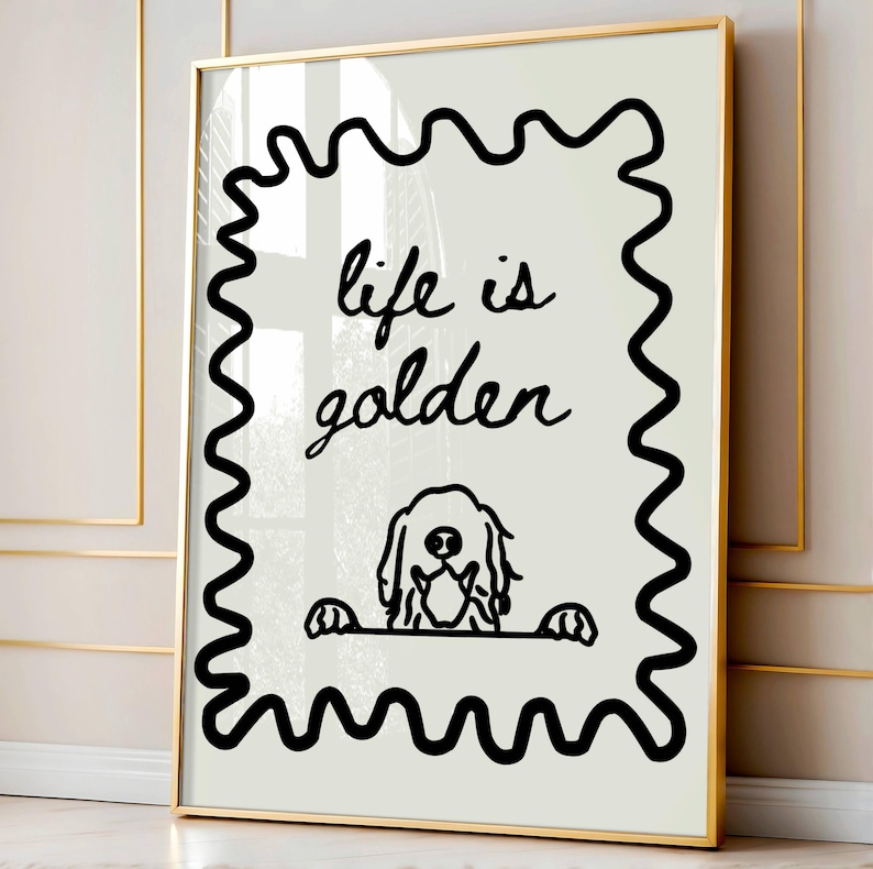 May include: A framed wall art print featuring a cream-colored background with a black wavy border. The text "life is golden" is written in a black cursive script above a simple black line drawing of a dog peeking over a horizontal line.
