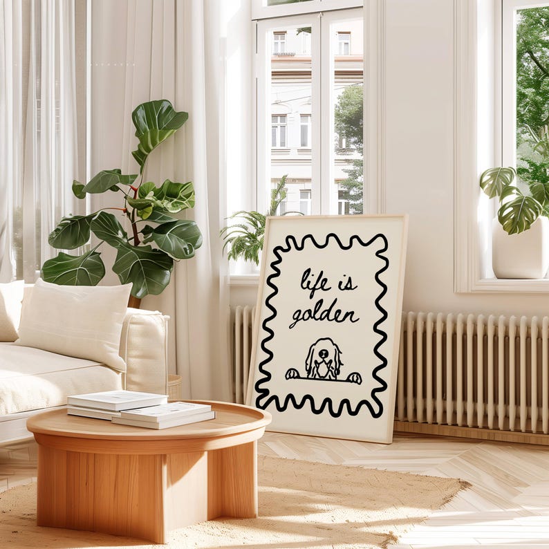 May include: A rectangular framed wall art print featuring a black wavy border on a cream background. The text "life is golden" is written in a black cursive script above a simple line drawing of a dog peeking over a horizontal line.