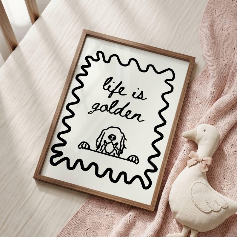 May include: A rectangular wall art print in a thin brown wooden frame featuring a black line drawing of a dog peeking over a wavy border with the handwritten text "life is golden" centered above the dog on a plain white background.
