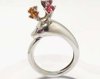 May include: A silver ring with a deer head design. The deer has antlers with orange and pink gemstones.