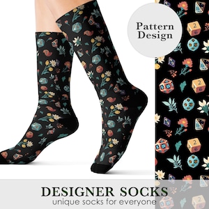 May include: Black designer socks with a floral and dice pattern. The socks feature a repeating design of flowers, dice, and other game-related elements in shades of orange, yellow, and blue. The text "DESIGNER SOCKS unique socks for everyone" is at the bottom.
