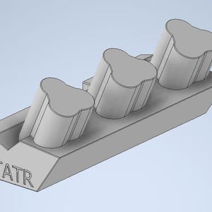May include: A light gray 3D-printed holder with three angled, cylindrical compartments, each topped with a unique, rounded shape. The base is rectangular with the letters "TATR" embossed on the side.