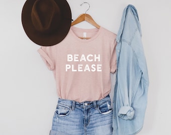 May include: A pink t-shirt with the text "Beach Please" in white lettering. The shirt is paired with denim shorts and a light blue denim jacket. A brown fedora hat is also included.