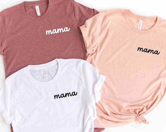 以下が含まれることがあります： 「ママ」という単語が筆記体で書かれた3枚のTシャツ。Tシャツは、マルーン、ピーチ、白の3色です。