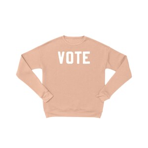 Peut inclure: Un sweat-shirt couleur p&ecirc;che avec le mot "VOTE" imprim&eacute; en blanc sur le devant.
