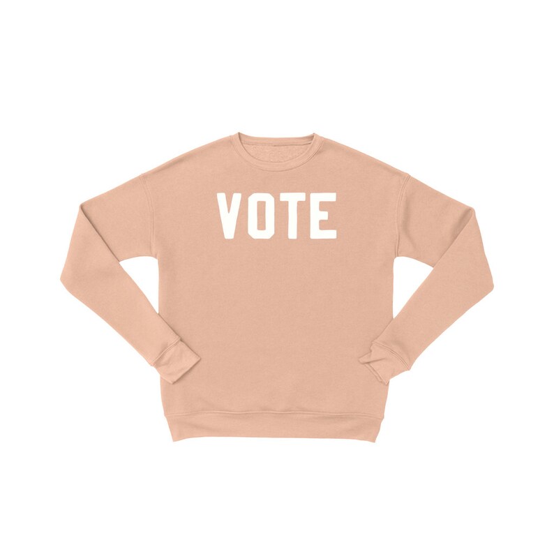 Peut inclure: Un sweat-shirt couleur p&ecirc;che avec le mot "VOTE" imprim&eacute; en blanc sur le devant.
