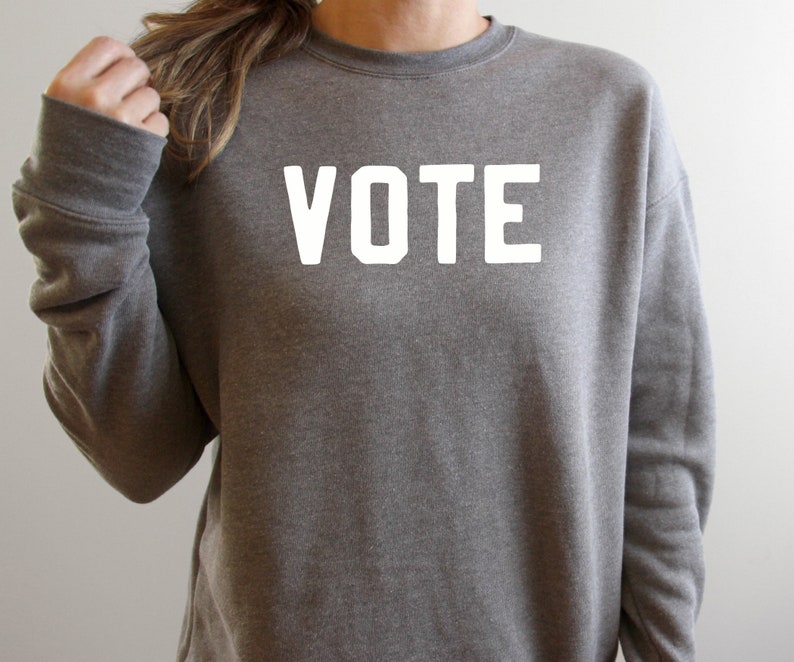 Peut inclure: Un sweat-shirt gris avec le mot "VOTE" imprim&eacute; en blanc sur le devant.