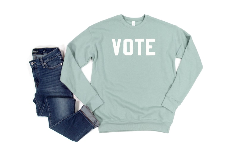 Peut inclure: Un sweat-shirt bleu clair avec le mot "VOTE" imprim&eacute; en blanc sur le devant. Le sweat-shirt est associ&eacute; &agrave; un jean bleu.