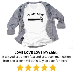 May include: White t-shirt with a black hammer graphic and the text "THIS IS NOT A DRILL!" printed on it.