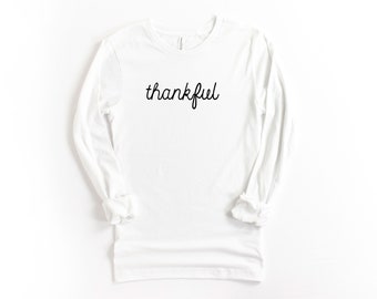May include: White long-sleeve t-shirt with the word "thankful" written in black cursive script.