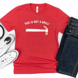 May include: Red t-shirt with white text that says "This is not a drill!" and a white outline of a hammer.