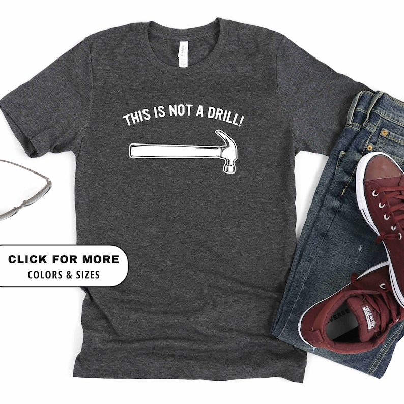 May include: A dark heather grey t-shirt with a white graphic of a hammer and the text "This is not a drill!"