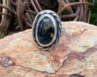 May include: A silver ring with a black and gold oval gemstone set in a braided silver band.