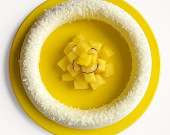Pode incluir: Um prato amarelo com um anel de coco branco e um monte de abacaxi em cubos no centro.