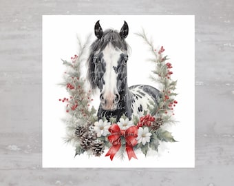 May include: A black and white spotted horse with a black mane and tail is framed by a green wreath with red berries and a red bow. The horse is looking directly at the viewer.