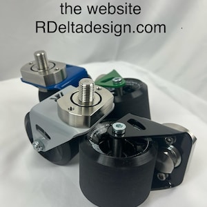 May include: Four caster wheels in blue, grey, green, and black. Each wheel has a black cylindrical base and a metal top with a threaded bolt. The text "More colours available on the website RDeltaDesign.com" is at the top.