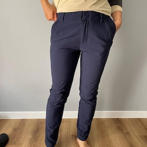 Pode incluir: Calças azul marinho com corte sob medida. As calças têm um design clássico com bolsos frontais e fecho de botão. O tecido parece ser um material liso e resistente a rugas. As calças são usadas com uma camisa bege e cinza de manga comprida.