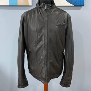 May include: A dark brown leather jacket with a full-length zipper, a small chest pocket, and a stand-up collar. The jacket is displayed on a mannequin and appears to be a medium size.