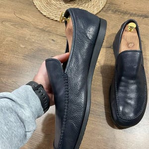 May include: Navy blue leather loafers with a rounded toe and stitched vamp. The shoes are displayed on a wooden surface. The loafers have a flat sole.