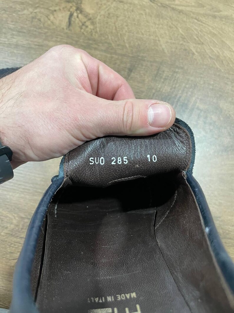May include: Close-up of the interior of a navy blue leather shoe. The shoe's insole is brown with the text "SUO 285" and the number "10" printed on it. The words "MADE IN ITALY" are visible.