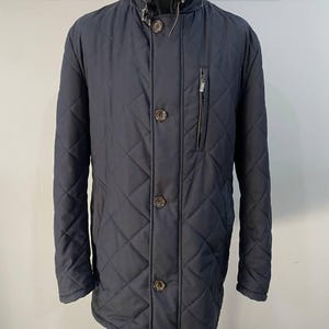 May include: Navy blue quilted jacket with a high collar and button closure. The jacket features a diamond pattern, a zippered chest pocket, and brown buttons. A stylish outerwear piece for cooler weather.