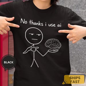 May include: A black short-sleeved t-shirt featuring a white graphic of a stick figure pointing at a brain. Above the figure, the text reads "No thanks i use ai" in a simple white font. The design is centred on the front of the shirt.