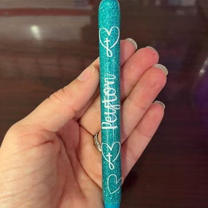 May include: Teal glitter pen with a white heart and cross design and the word "Peterson" written on the side.