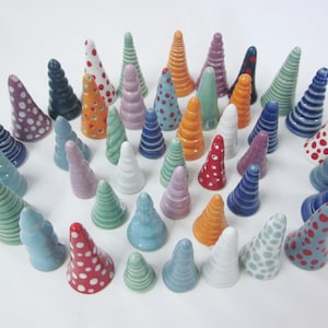 May include: A collection of 30 ceramic ring holders in various colors and patterns, including stripes, polka dots, and swirls. The holders are cone-shaped and arranged in a circle on a white surface.