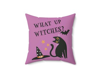 May include: A square throw pillow in a light purple color featuring the text WHAT UP WITCHES? in black letters. The design includes a black cat, a black witch hat with white stars, three small yellow stars, and a small black bat silhouette.