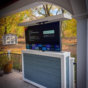 May include: A white and blue outdoor TV cabinet with a white frame and a retractable TV screen. The TV screen is displaying the Google TV home screen with the text "The entertainment you love".