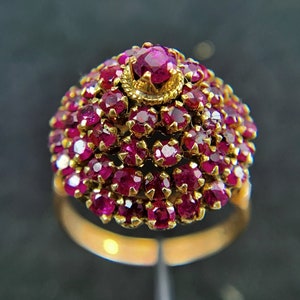 May include: A gold ring with a large, dome-shaped cluster of ruby red stones.