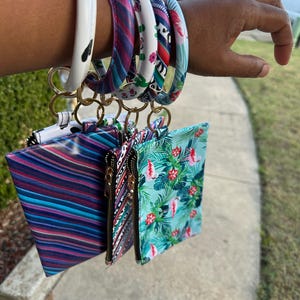 May include: A collection of colorful silicone bracelets and matching zippered pouches. The bracelets feature various patterns, including a cow print, stripes, and floral designs. The pouches have coordinating patterns and gold-tone zippers.