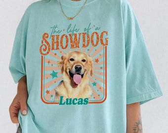 Puede incluir: Camiseta azul claro con un gráfico de un Golden Retriever y el texto "the life of a SHOWDOG" y el nombre "Lucas". El diseño incluye estrellas y un marco de estilo retro.