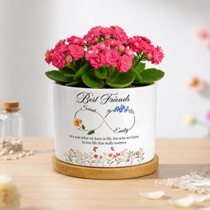 May include: A white ceramic planter containing a vibrant pink Kalanchoe plant. The pot features an infinity symbol graphic with the text Best Friends, Sarah, and Emily, plus the quote It's not what we have in life, but who we have in our life that really matters.
